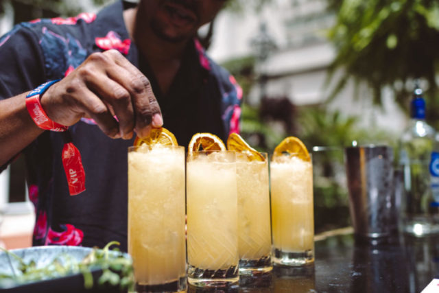 A bartender garnishing glasses of what appears to be a citrus-based cocktail with slices of orange.