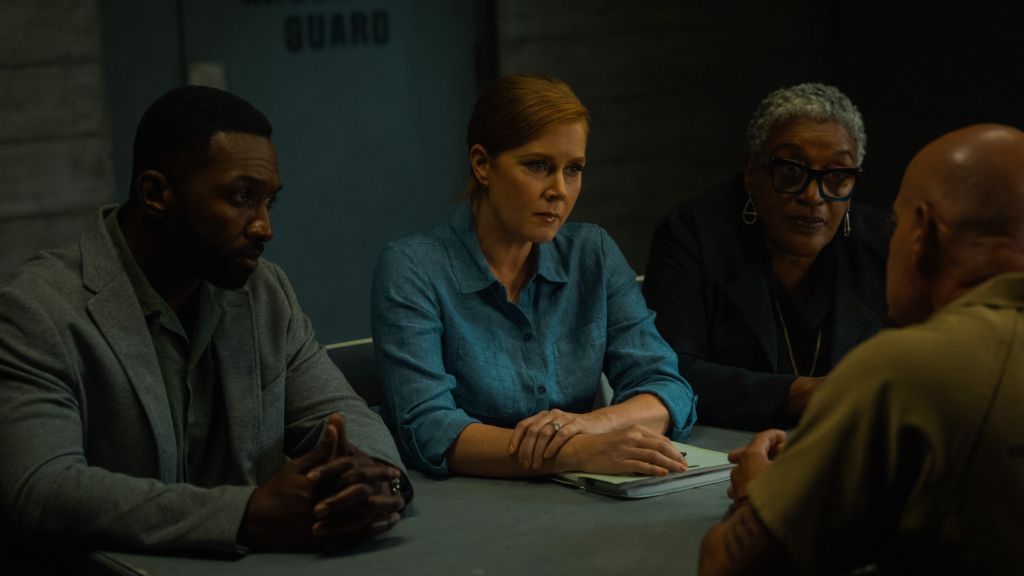 Four people sitting at a table in a dimly lit room, one person speaking to the others.