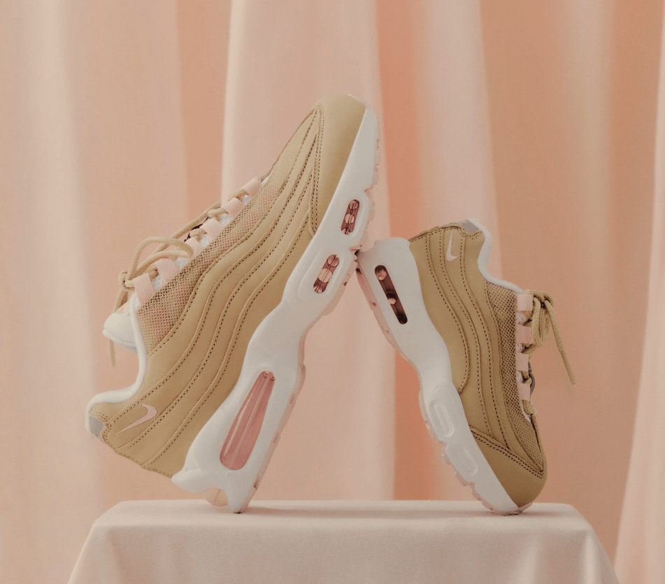 Pair of beige and white athletic shoes with pink accents, standing on a white surface against a pink background.