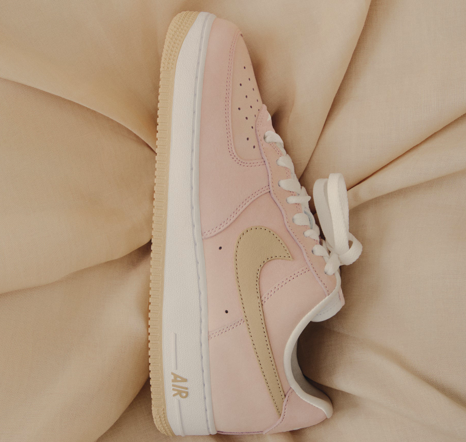 A pair of pink and white Nike Air Force 1 sneakers on a beige background.