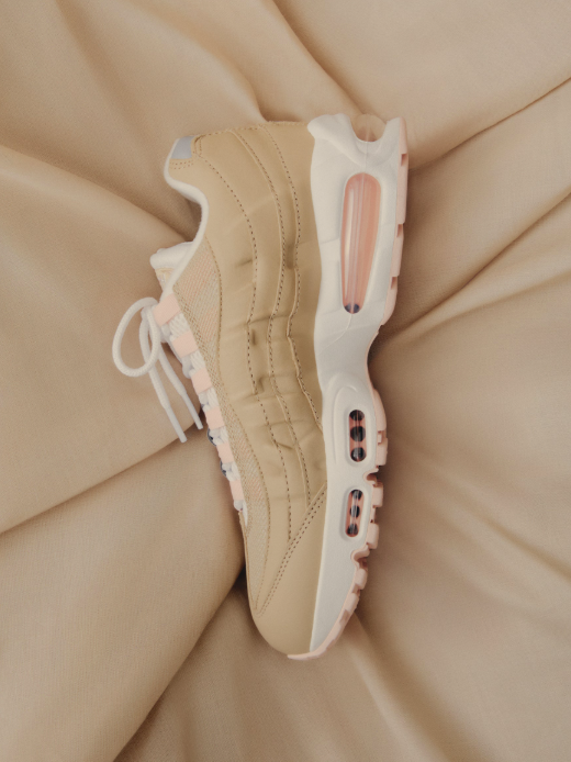 Beige sneakers with white soles and accents, resting on a soft, peach-colored fabric.