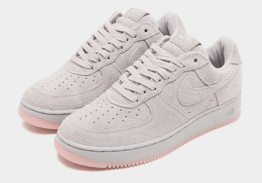 A pair of light gray Nike Air Force 1 sneakers with light pink soles.