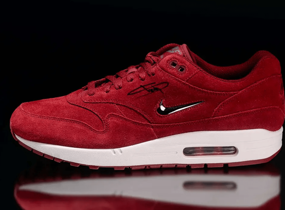 A red Nike Air Max 1 sneaker with a white sole and Nike logo on a black background.