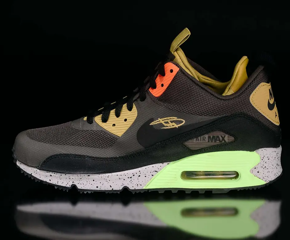 A pair of Nike Air Max 90 sneakers in a dark gray, orange, and neon green color scheme with the Nike logo visible.