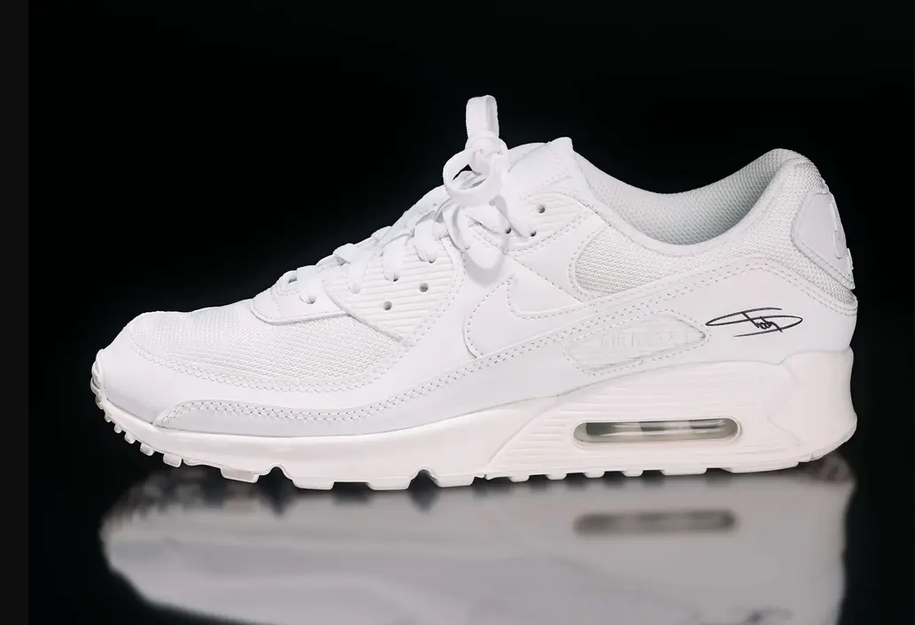 White Nike Air Max 90 sneakers on a reflective surface against a black background.