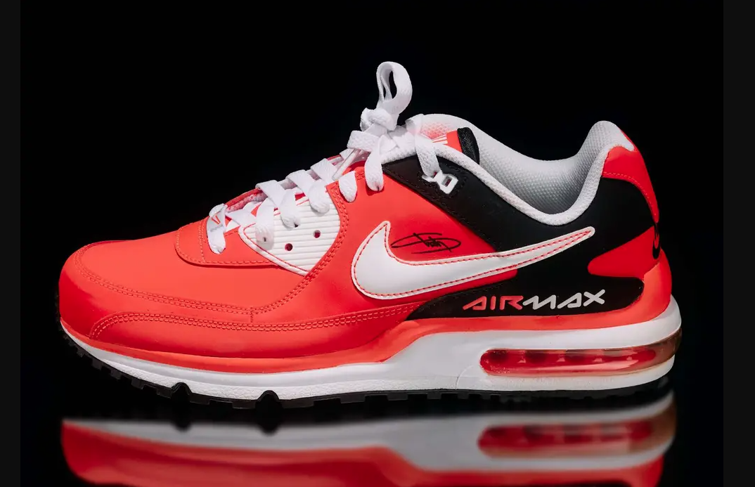 A pair of bright red Nike Air Max sneakers with white and black accents, reflecting on a glossy black surface.