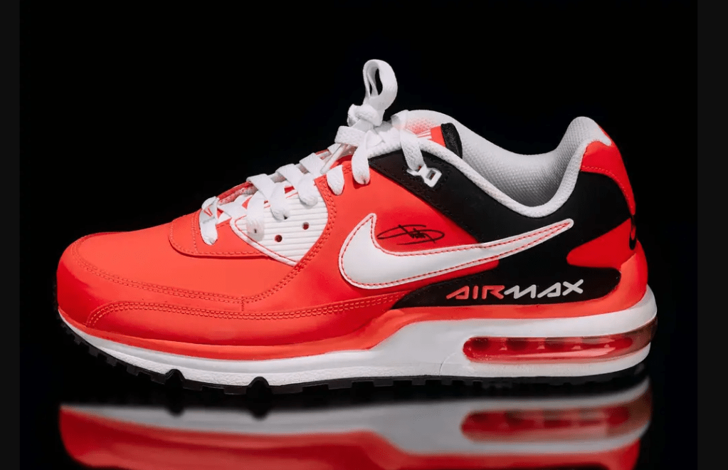 A pair of bright red Nike Air Max sneakers with white and black accents, reflecting on a glossy black surface.