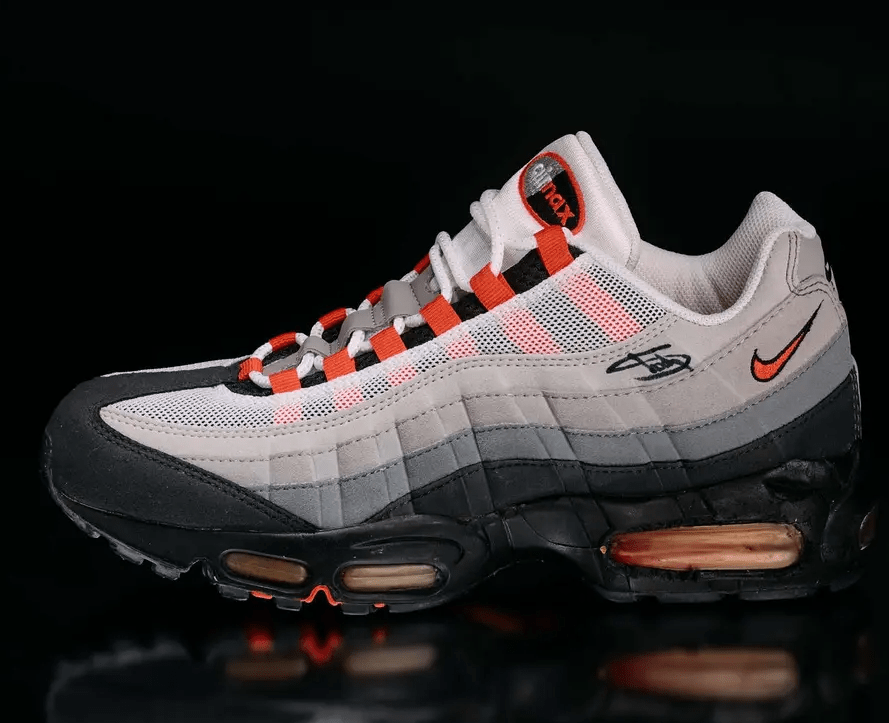 A pair of Nike Air Max 95 sneakers in gray, black, and orange, featuring a mesh upper and visible air cushioning.
