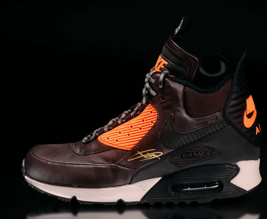 A pair of Nike Air Max 90 sneakers in a dark brown and orange color scheme, featuring the Air Max branding and visible air cushioning.