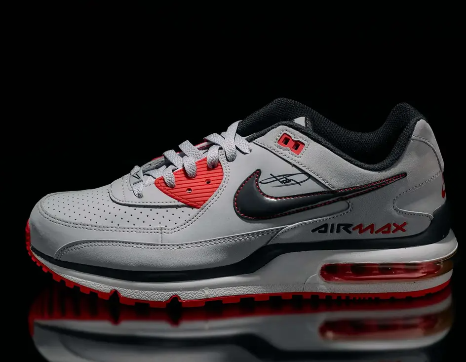 A pair of gray and red Nike Air Max sneakers with black accents, displayed against a black background.
