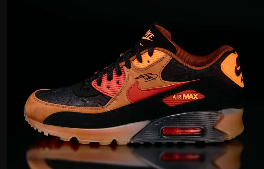 A pair of Nike Air Max 90 sneakers in black, orange, and red colors with the Air Max branding visible.