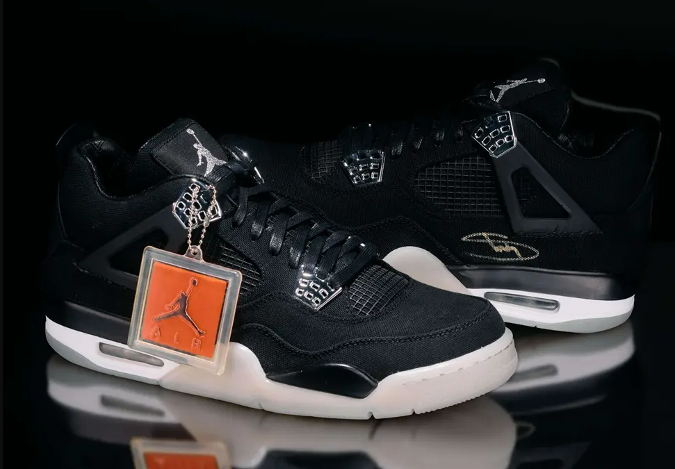 Black and white Nike Air Jordan 4 sneakers with orange accents and a Jordan brand logo.