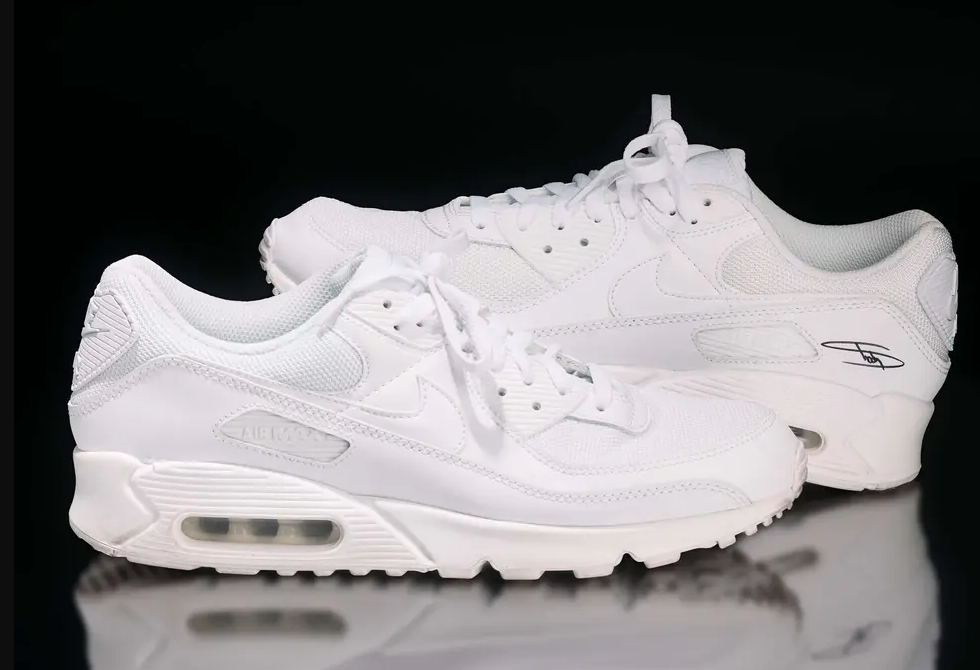 A pair of pristine white Nike Air Max 90 sneakers against a dark background.