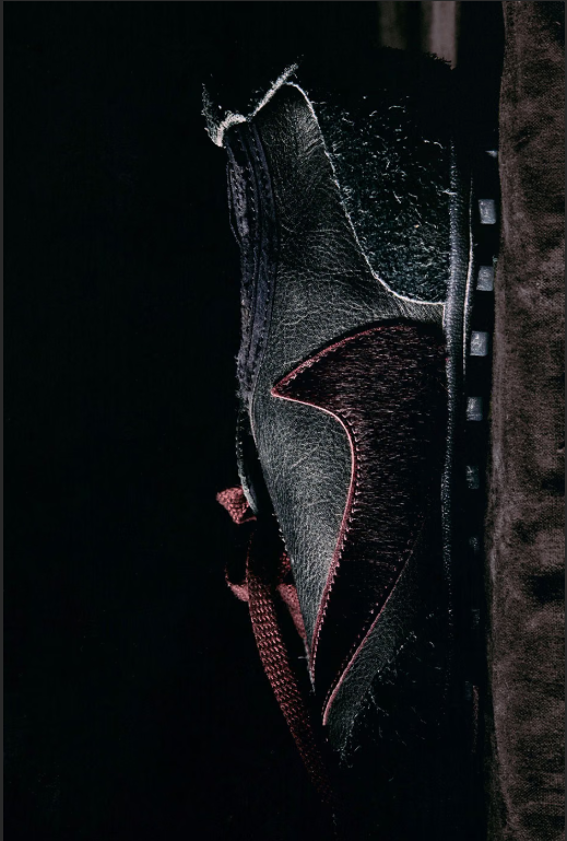 A close-up view of a black leather boot with a red sole and stitching.