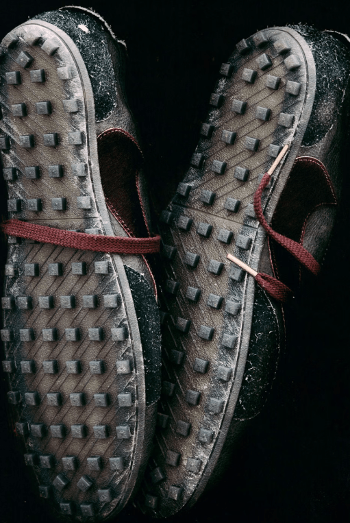 Pair of worn, muddy hiking boots with deep tread patterns and red laces against a dark background.