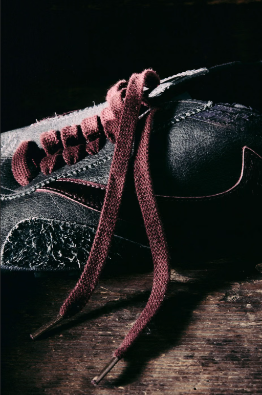 A close-up view of a black leather boot with pink laces and a textured sole on a wooden surface.
