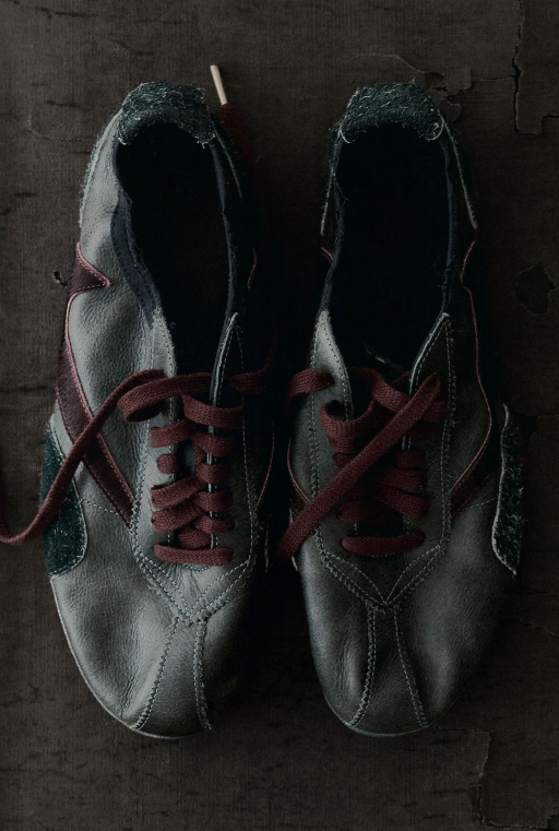 A pair of black leather shoes with burgundy laces, resting on a dark, textured surface.
