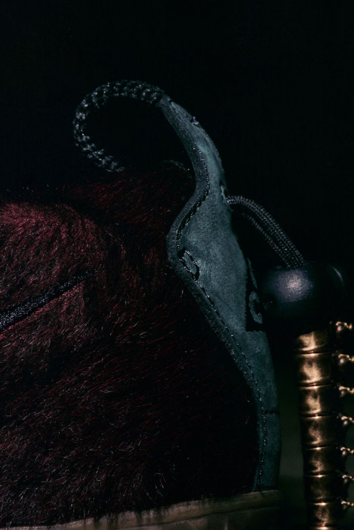 A dark, close-up view of a black snake with a distinctive pattern on its body, coiled against a dark, textured background.