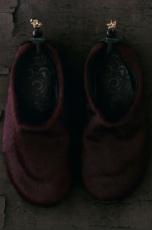 Two dark, ornate, fur-lined boots with intricate patterns against a dark background.