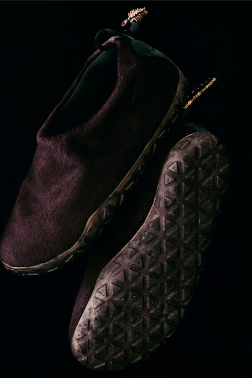 A close-up view of a dark-colored shoe with a distinctive tread pattern and laces.