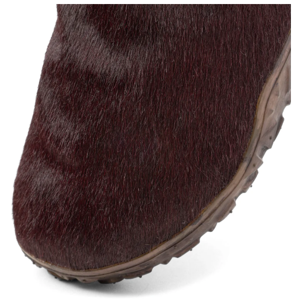 Close-up of a dark brown, furry boot with a textured sole.