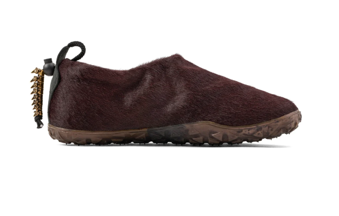 A pair of dark brown furry slippers with a black strap and gold-colored studs.