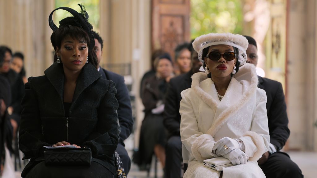 Two women in formal attire walking together, one in a black coat and the other in a white fur coat and hat.