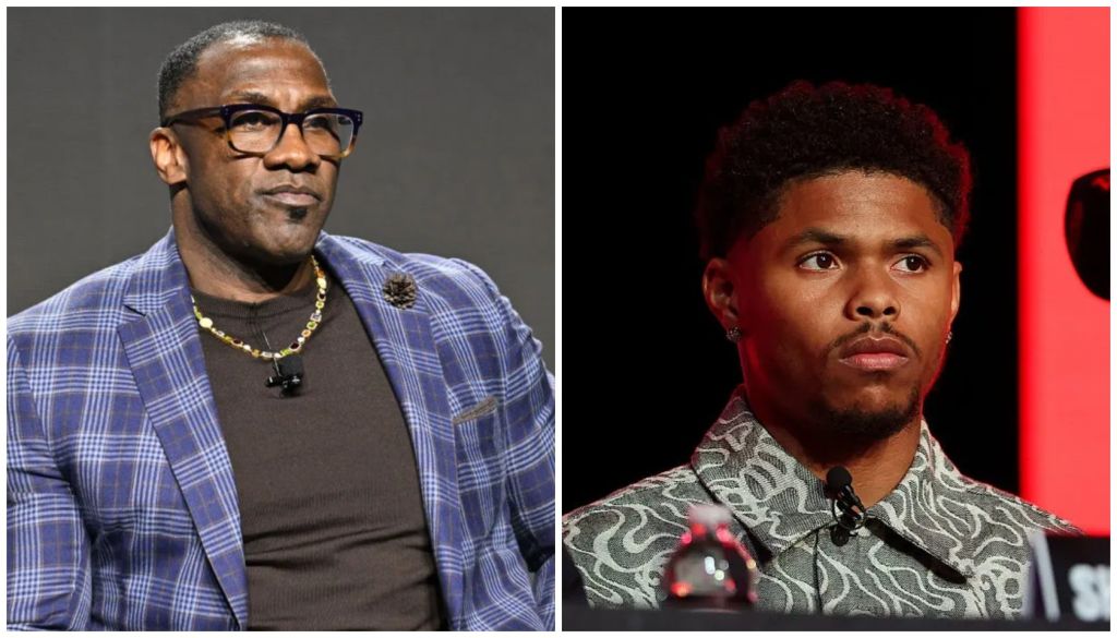 Two Black men in formal attire on stage, one wearing glasses and a plaid jacket, the other in a patterned jacket.