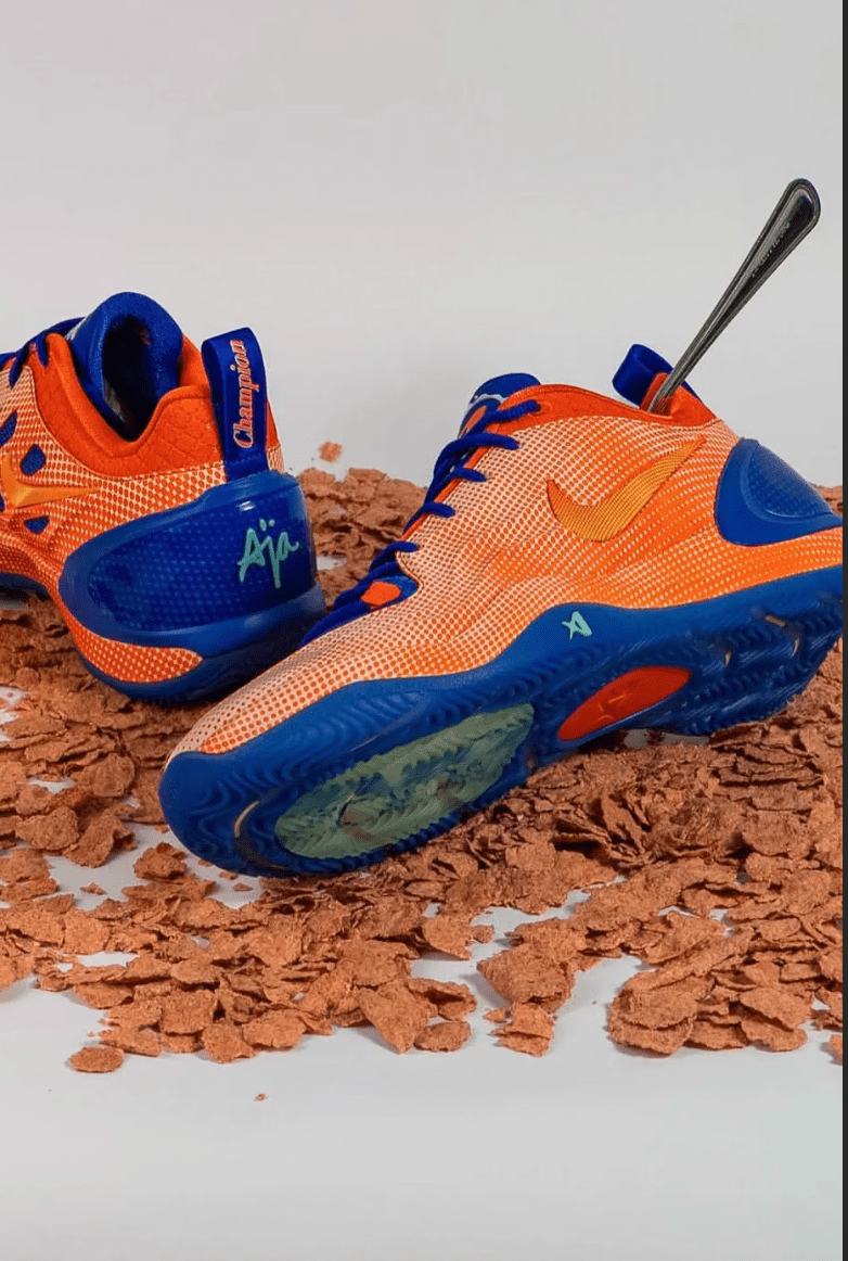 Pair of orange and blue athletic shoes with the "Aja" logo, resting on a surface of crushed cereal.