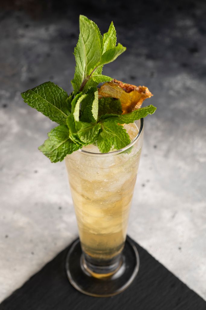 A glass of golden-colored beverage garnished with a sprig of fresh mint leaves.