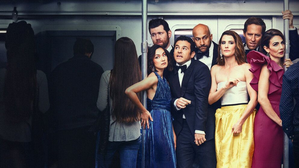 A group of people dressed formally posing together, including a man in a tuxedo and several women in colorful dresses.