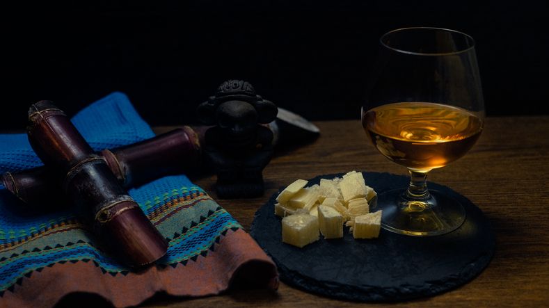 Glass of cane rum with pieces of cane on rustic wooden table and dark background