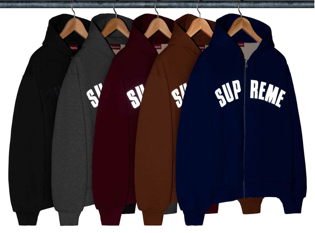 Assorted hoodies and sweatshirts hanging on a rack, with the text "SUP" and "REME" printed on them in various colors including black, gray, burgundy, brown, and navy blue.