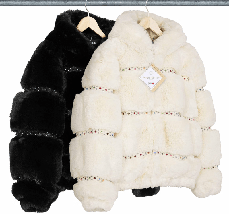 Two fur coats hanging on a rack, one black and one white with colorful beaded embellishments.