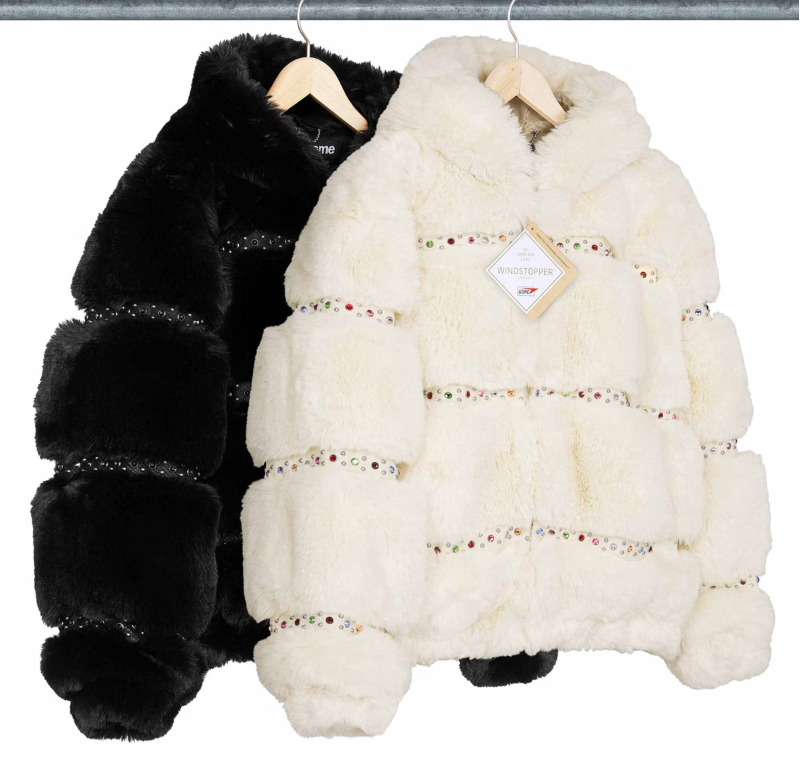 Two fur coats hanging on a rack, one black and one white with colorful beaded embellishments.
