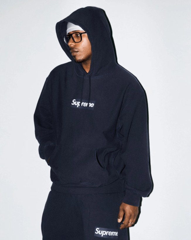 A person wearing a black hooded sweatshirt with the text "Supreme" printed on it.