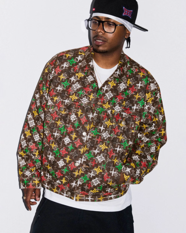 A person wearing a black hat with a logo, glasses, and a colorful patterned jacket.
