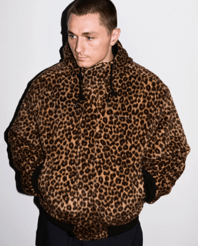 A person wearing a brown leopard print jacket standing against a white background.
