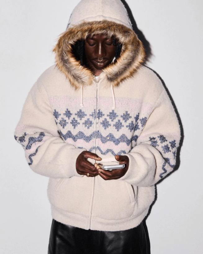 A person wearing a hooded, patterned sweater and holding a mobile device.