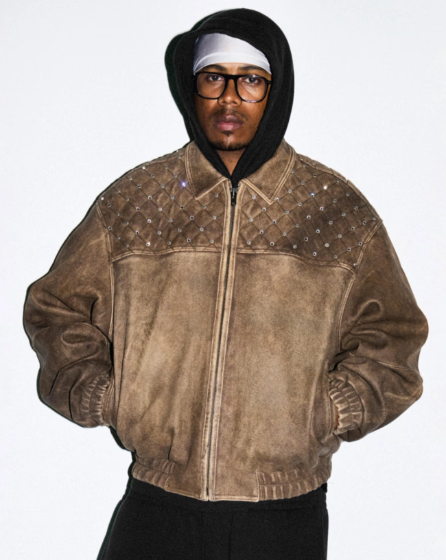 A person wearing a hooded jacket with a quilted pattern and glasses, standing against a plain background.