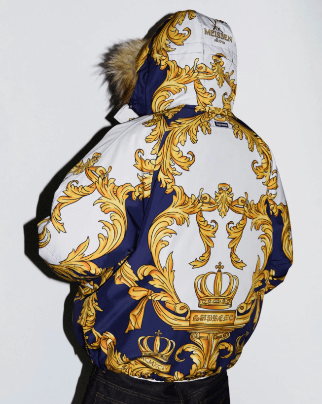 A person wearing a hooded jacket with a large, ornate, gold and blue printed design featuring a crown and floral patterns.