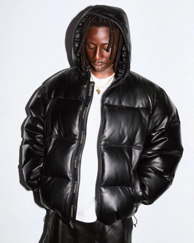 A person wearing a black hooded jacket with a zipper and pockets, standing against a plain white background.