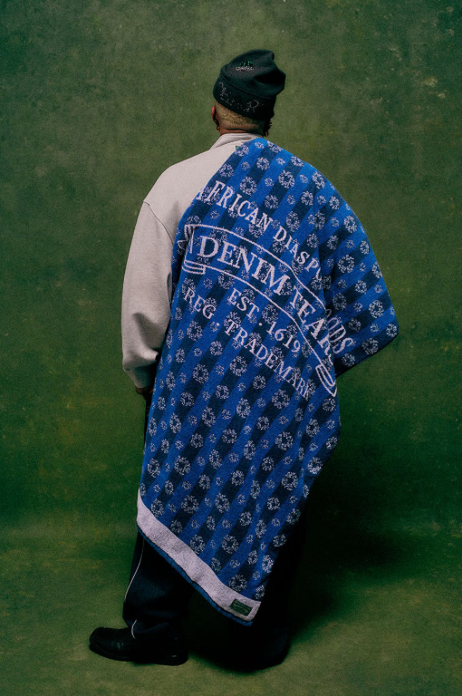 A person wearing a blue and white patterned African diaspora denim jacket, standing in front of a green background.