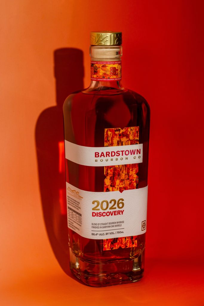 A bottle of Bardstown Bourbon Co. 2026 Discovery, a blend of straight bourbon whiskeys finished in Bardstown oak barrels, against a vibrant orange background.