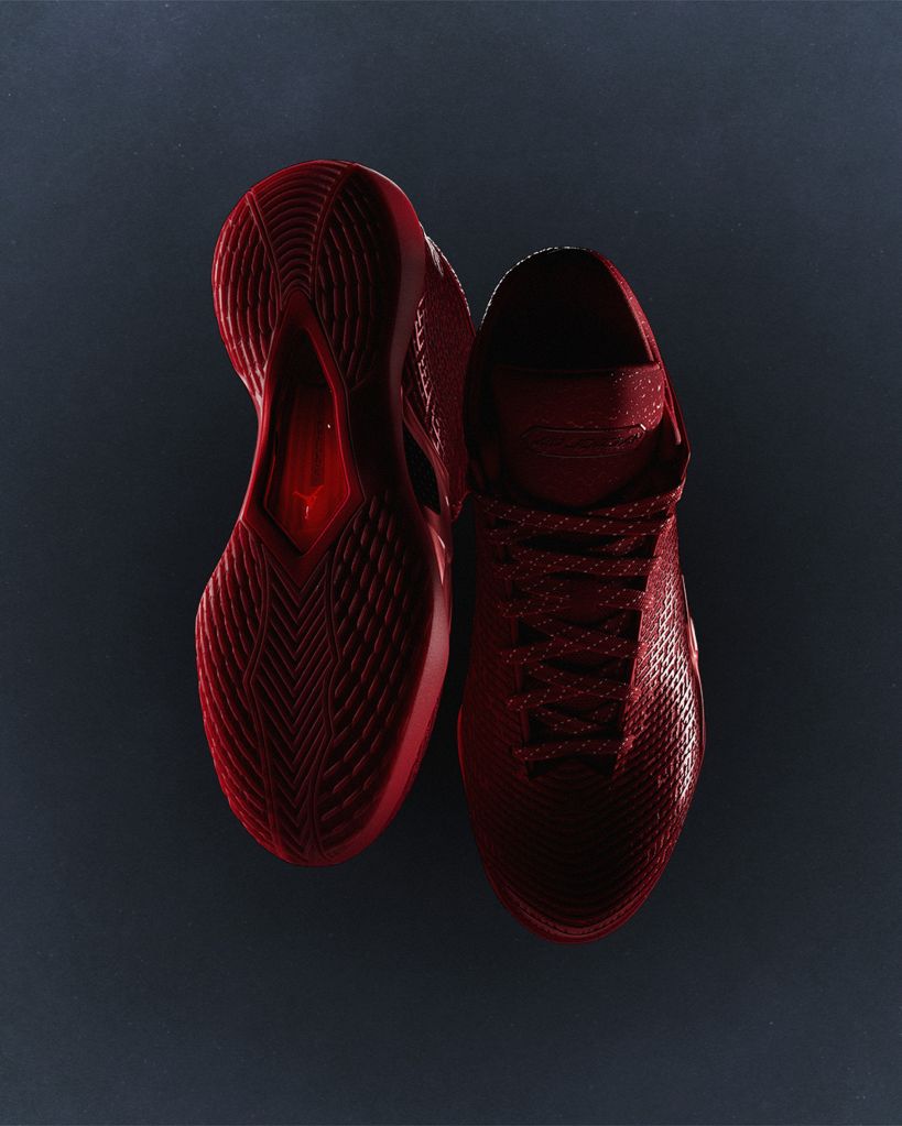 A pair of red athletic shoes with a textured pattern and laces against a dark background.