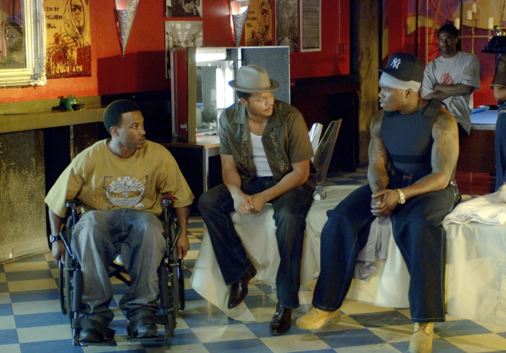 Three men sitting in a room with posters and memorabilia on the walls, one man in a wheelchair.